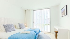 Een slaapkamer met een bed, twee nachtkastjes, een bureau en een groot raam met jaloezieën.