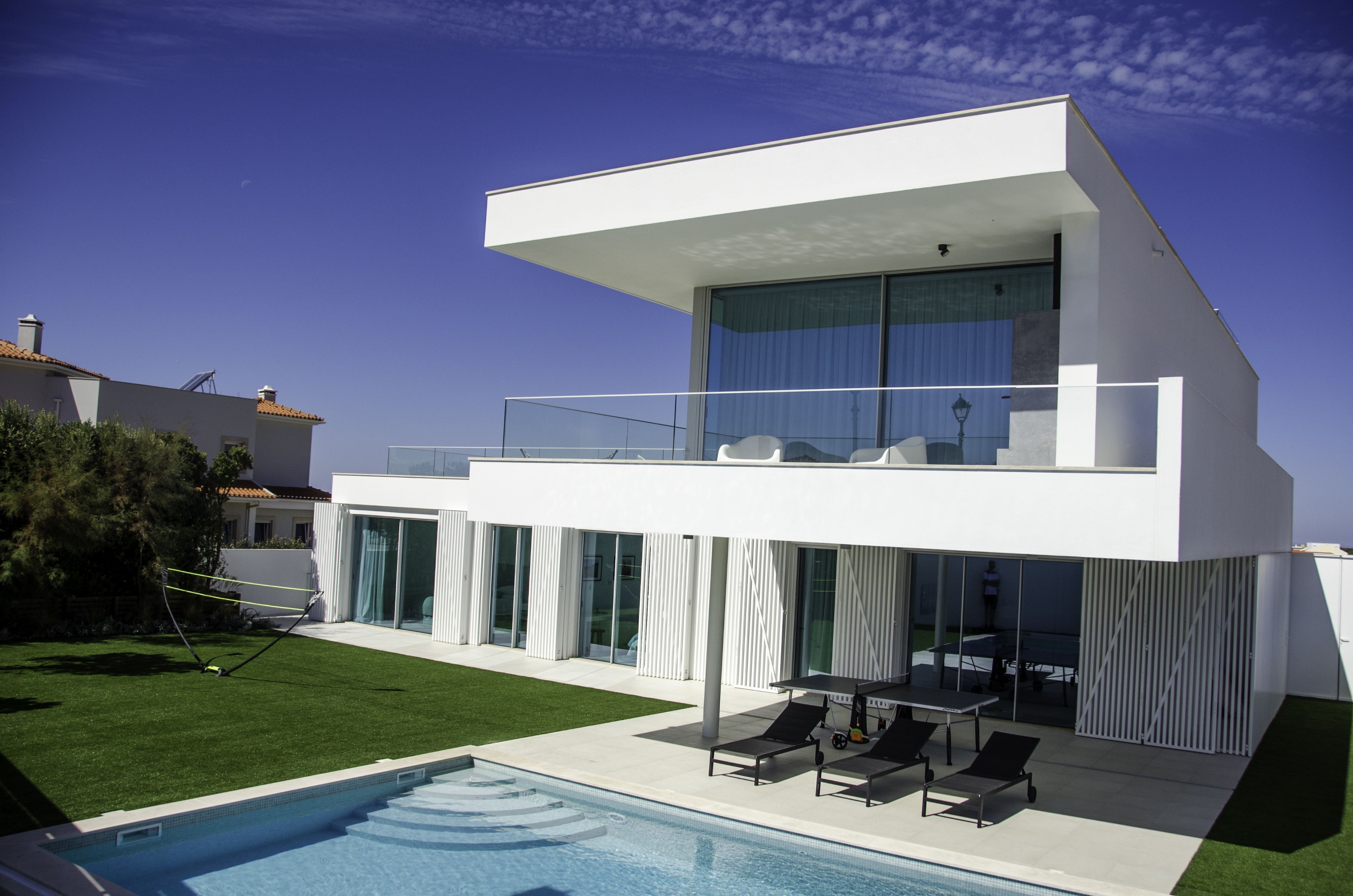 A modern two-story house with a swimming pool, large windows, and a balcony.
