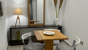 Ein moderner Essbereich mit einem Holztisch, zwei grauen Stühlen, einer Stehlampe, einem Spiegel und dekorativen Pflanzen.