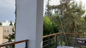 Ein Balkon mit Metallgeländer, Blick auf Bäume und ein Gebäude im Hintergrund.