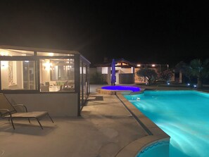 Una piscina amb vora blava, una zona de seients coberta amb cadires, i un edifici amb parets de vidre al fons.