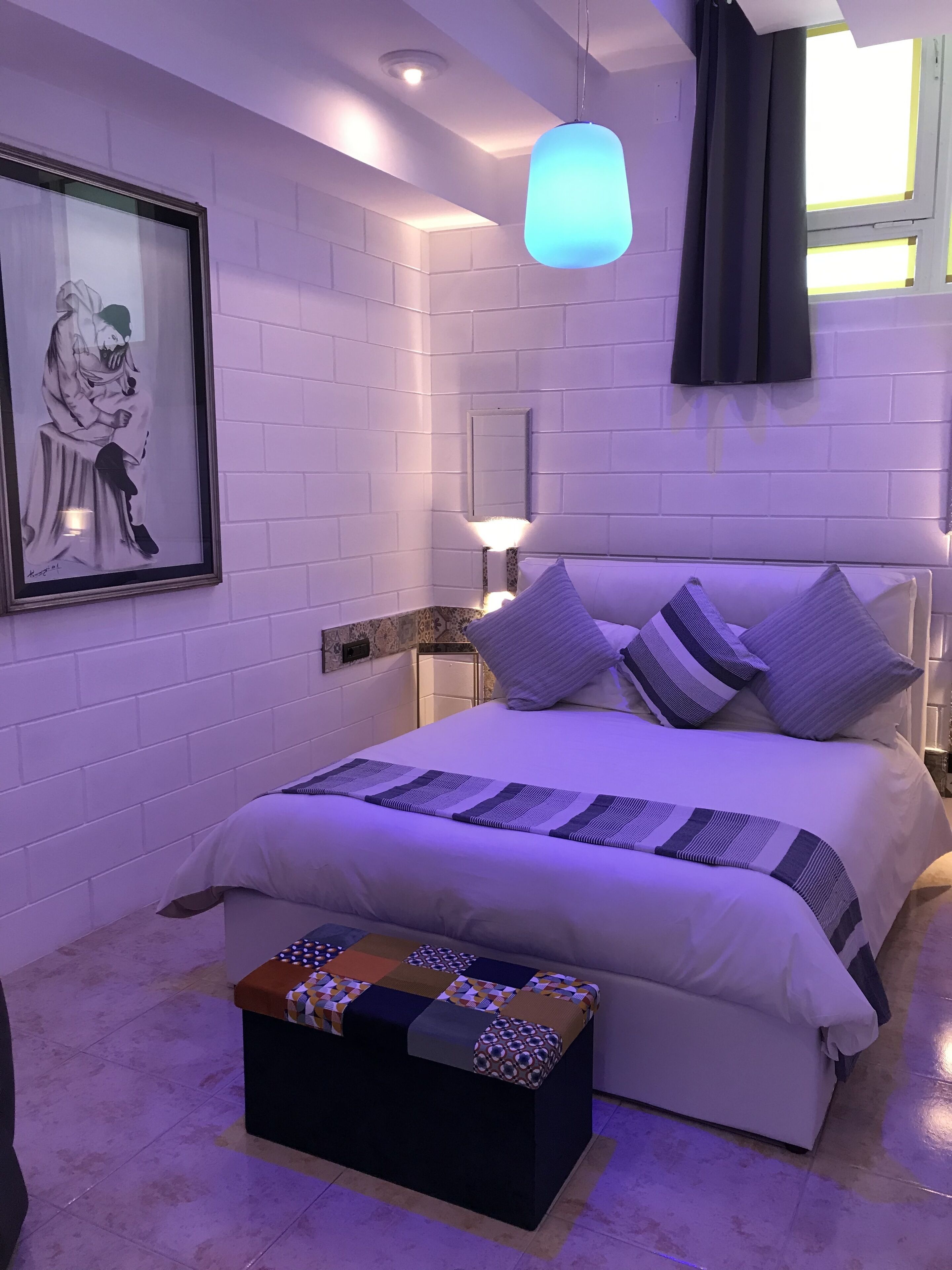 Une chambre à coucher moderne avec un grand lit, une table de chevet, une œuvre d’art encadrée et un luminaire suspendu.