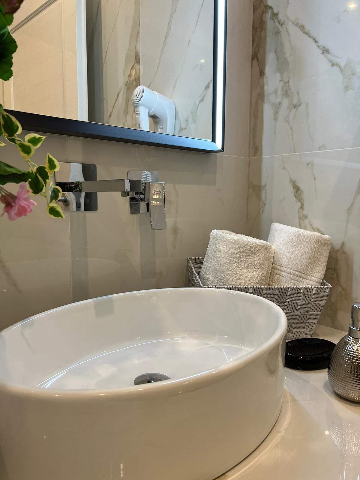 A bathroom with a large white sink, a mirror, a towel rack, and a wicker basket with towels.