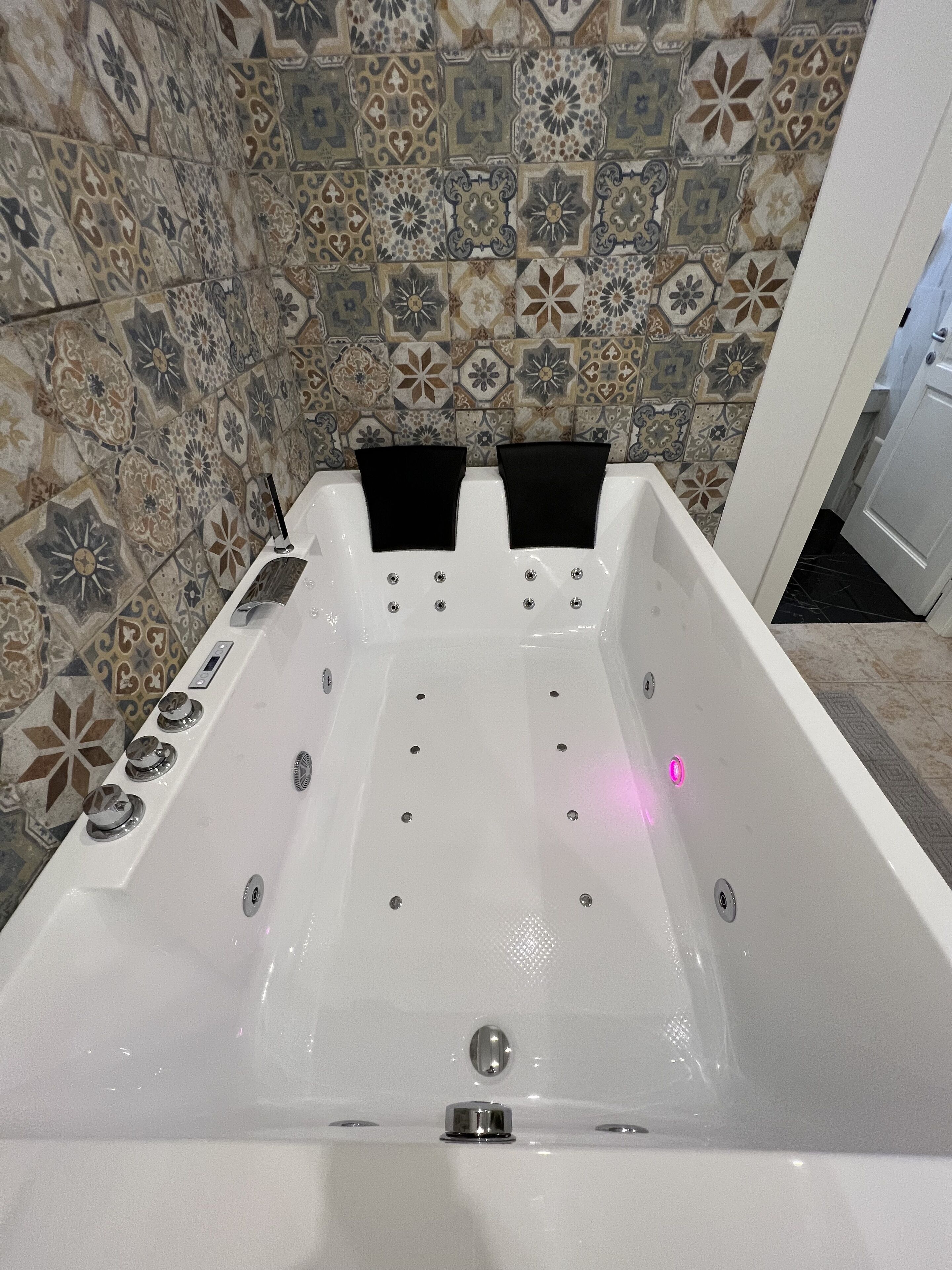 Une baignoire dotée d’un panneau de commande et d’une pomme de douche, placée devant un mur carrelé orné d’un motif floral.