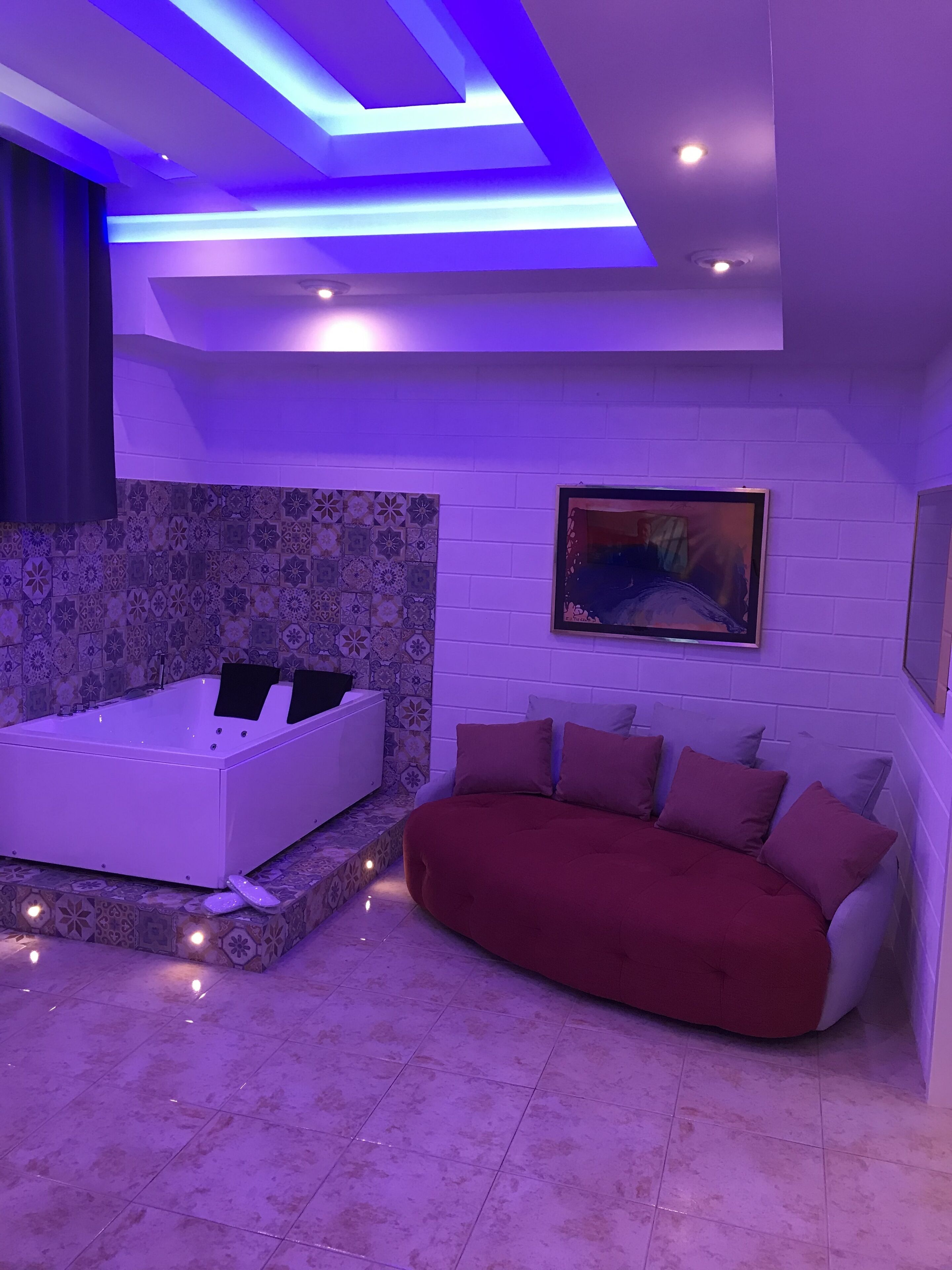A modern bathroom with a white bathtub, a red sofa, and a patterned tile wall.