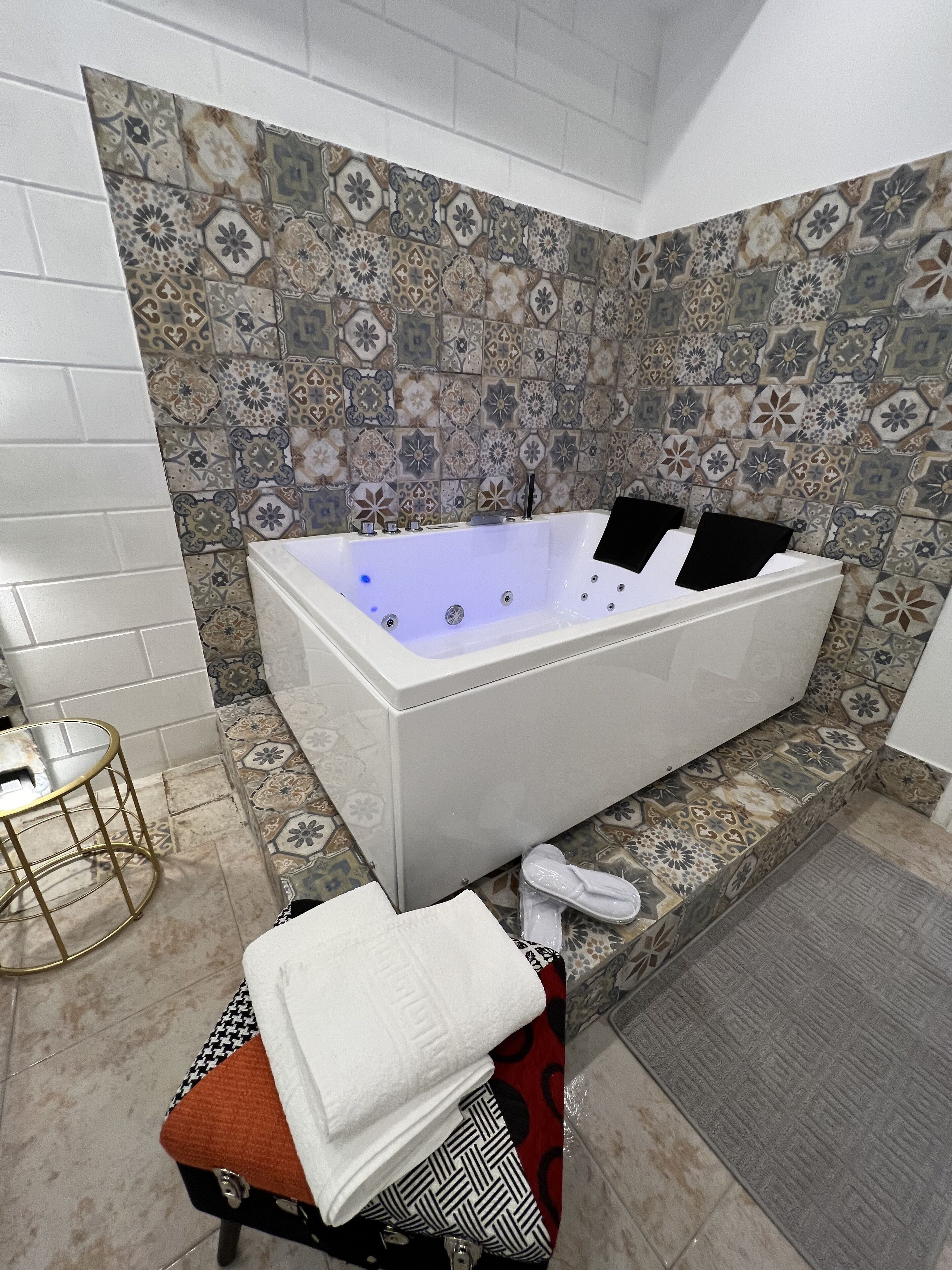A bathroom with a large bathtub, a small table, and a bench with towels.