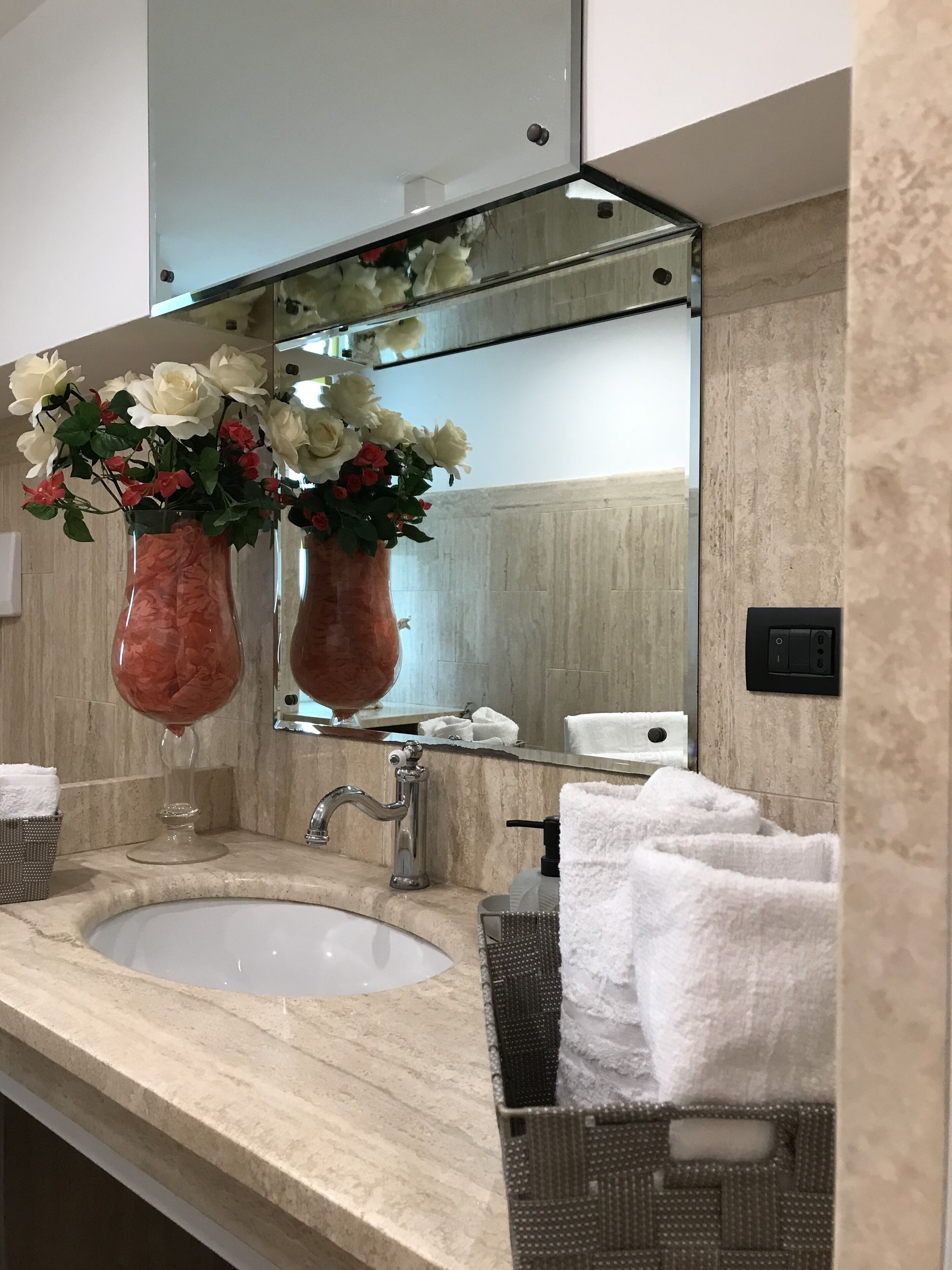 Une salle de bain avec un lavabo en marbre, deux vases en verre ornés de fleurs, un miroir et un porte-serviettes.
