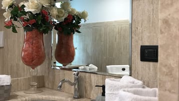 Une salle de bain avec un lavabo en marbre, deux vases en verre ornés de fleurs, un miroir et un porte-serviettes.