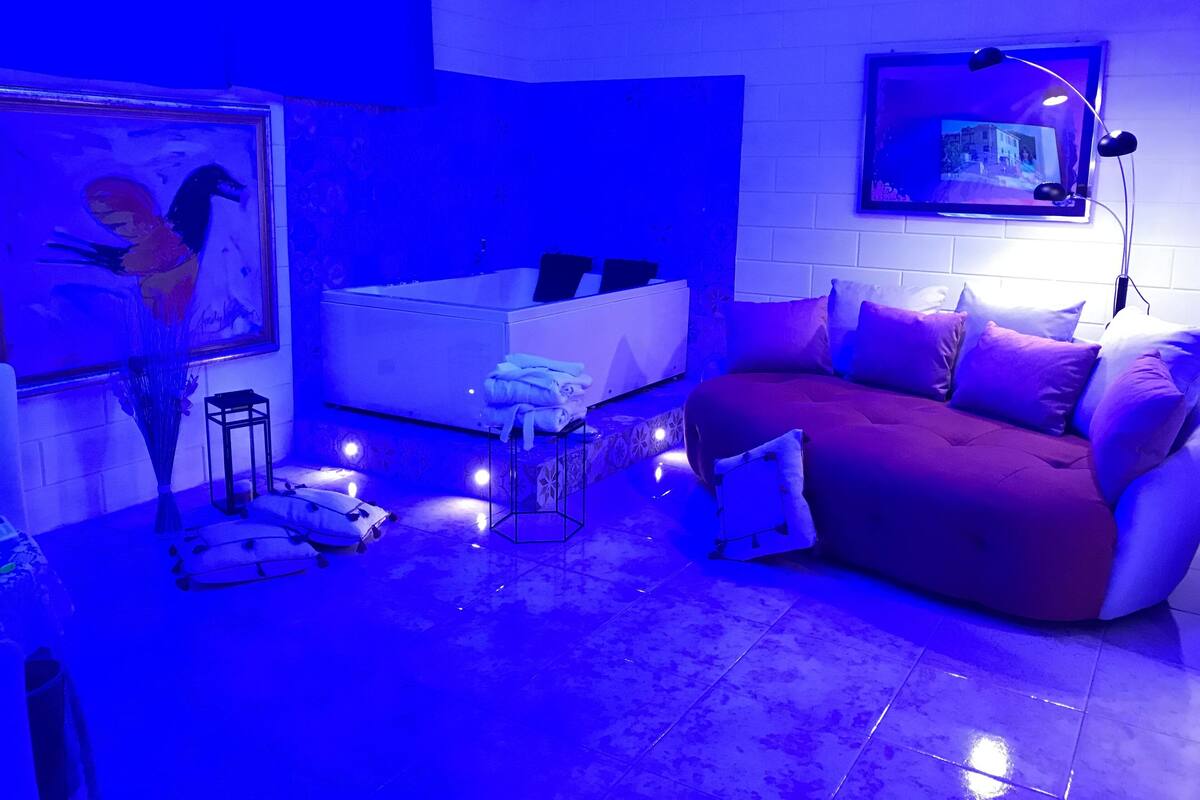 Una sala de estar moderna con una atmósfera azulada, una bañera blanca, un sofá con cojines y un cuadro en la pared.