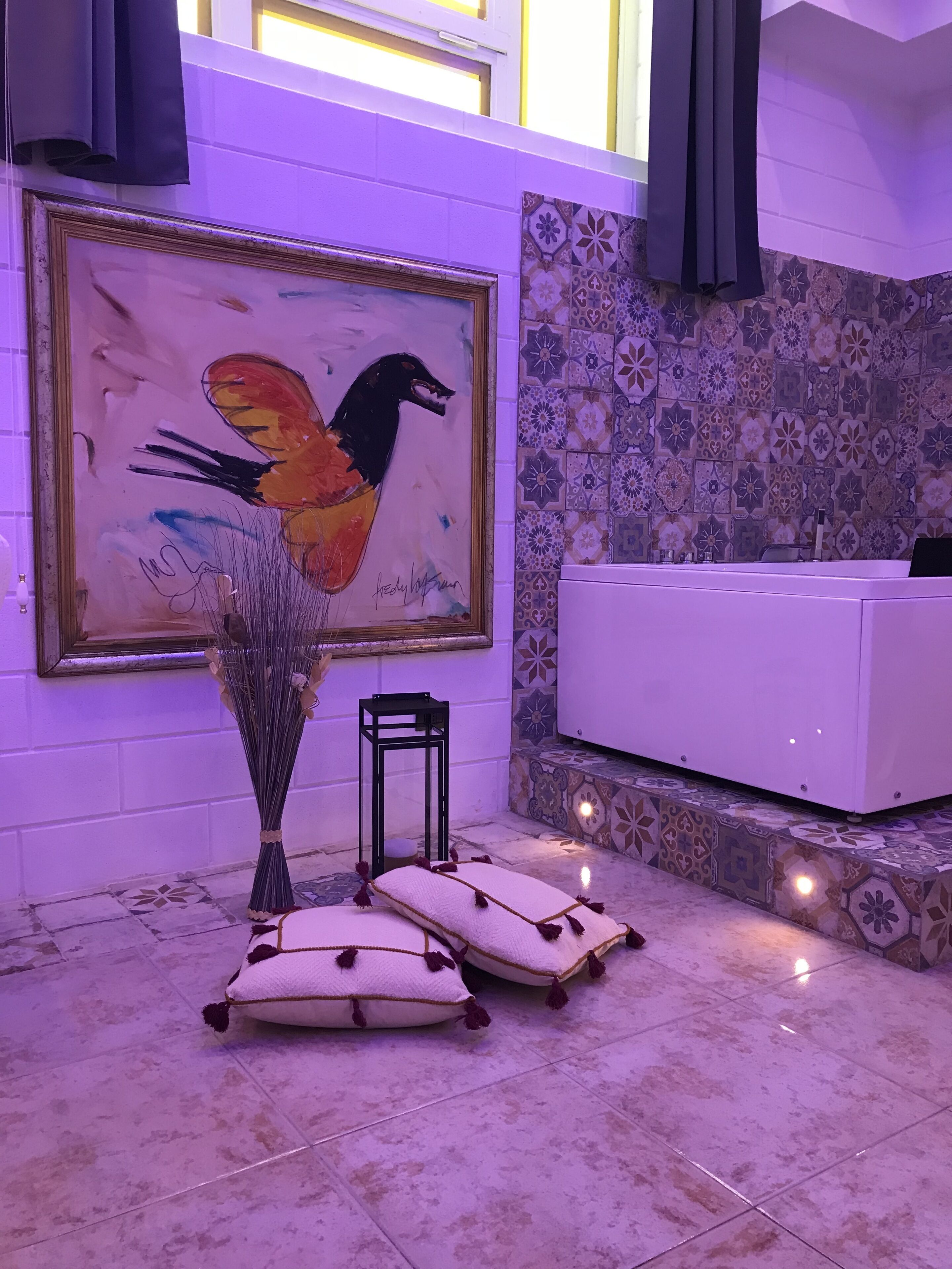 A bathroom with a bathtub, a painting, and a vase with dried plants.