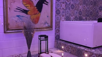 A bathroom with a bathtub, a painting, and a vase with dried plants.