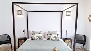 Een hemelbed met een groene sprei, twee nachtkastjes met lampen, en een decoratieve vaas op een houten kruk.