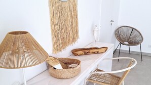 Een moderne, minimalistische kamer met een witte marmeren tafel, rieten stoelen, een ronde rieten stoel, een rieten lamp en een rieten mand.