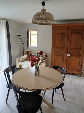 A dining area with a round table, chairs, a vase with flowers, a ceiling fan, a window, and a wooden cabinet.