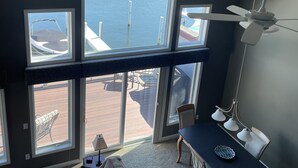 Ein Zimmer mit großem Fenster mit Blick auf eine Marina, einem Deckenventilator und einem Essbereich mit Tisch und Stühlen.