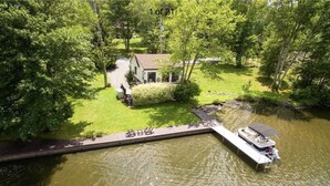 A house with a dock extending into a river, surrounded by greenery. - Charming Lake Front Cottage (Swan Lake)