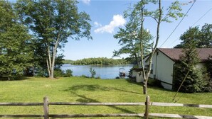 A lakeside property with a wooden fence, a small dock, and a house with a red roof. - Charming Lake Front Cottage (Swan Lake)