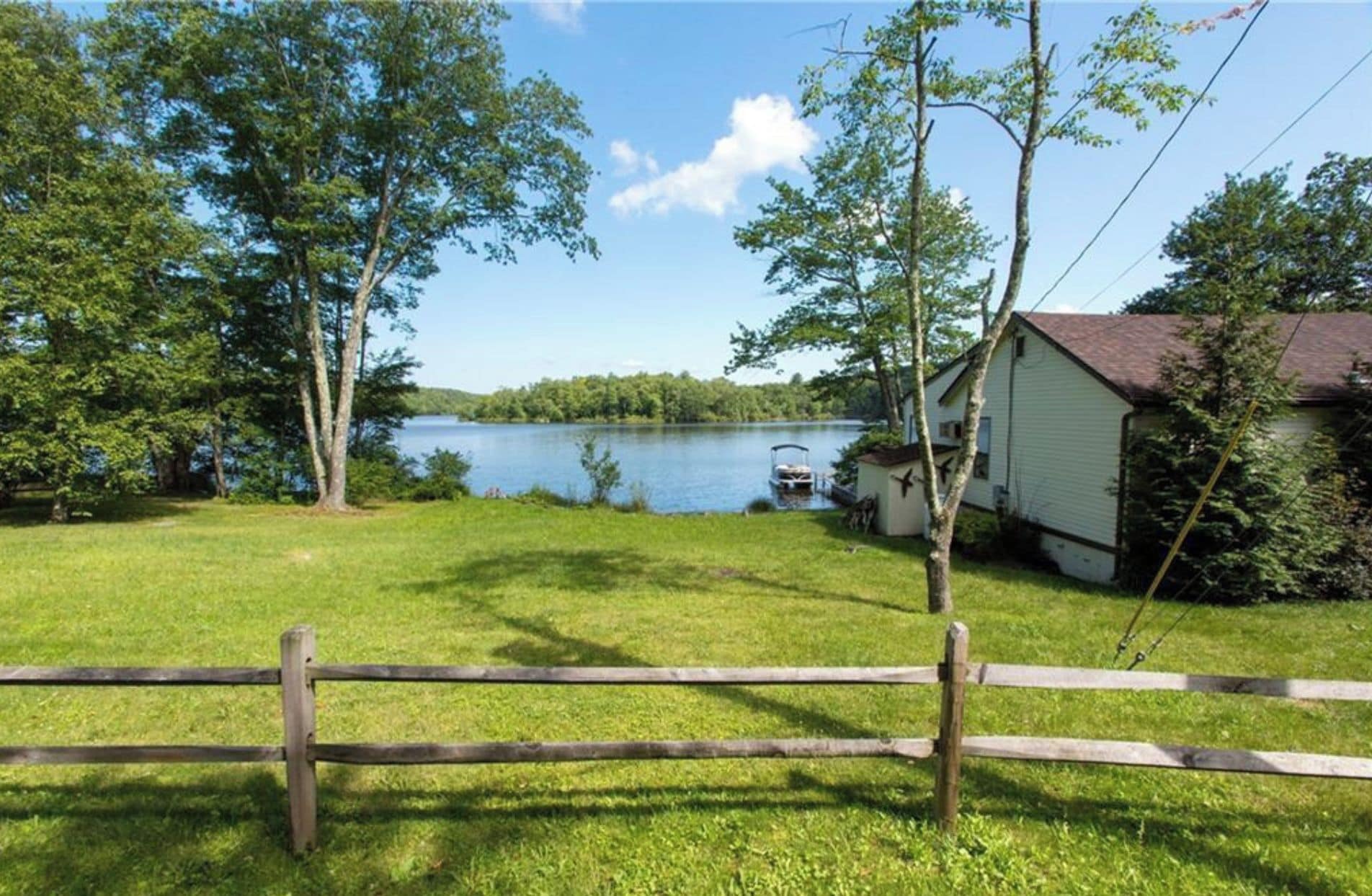 Une propriété au bord du lac, dotée d’une clôture en bois, d’un petit quai et d’une maison avec un toit rouge.