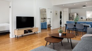 A modern living room with a flat-screen TV, wooden entertainment unit, grey sofa, and a dining area with a table and chairs. - Charming Lake Front Cottage (Swan Lake)