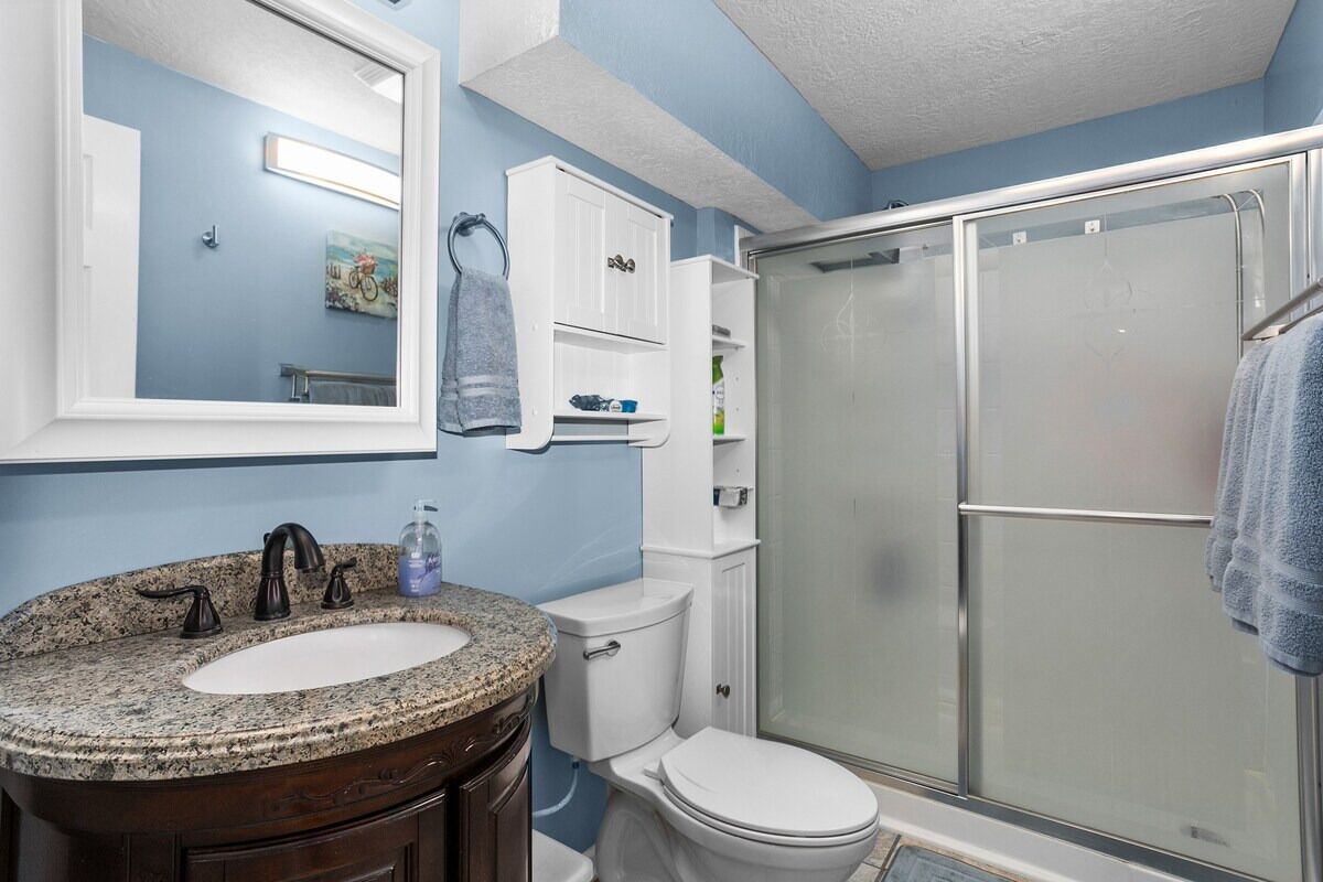 Baño con lavamanos de granito, inodoro blanco y cabina de ducha de vidrio.
