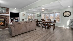 Un salon spacieux avec une cheminée, un coin repas avec une table et des chaises, et de grandes fenêtres.