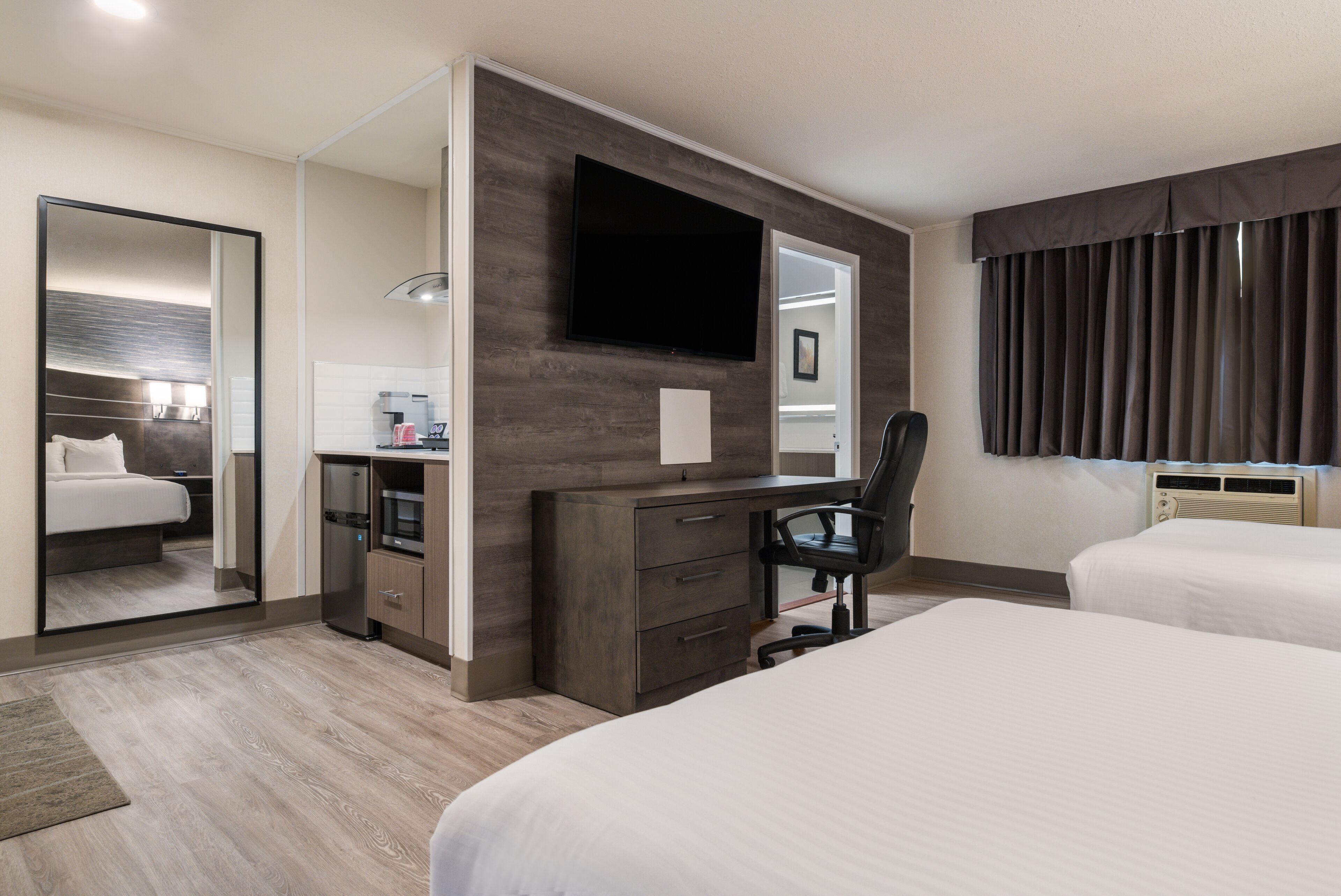 A hotel room with a bed, a desk with a chair, a flat-screen TV, and a large mirror.
