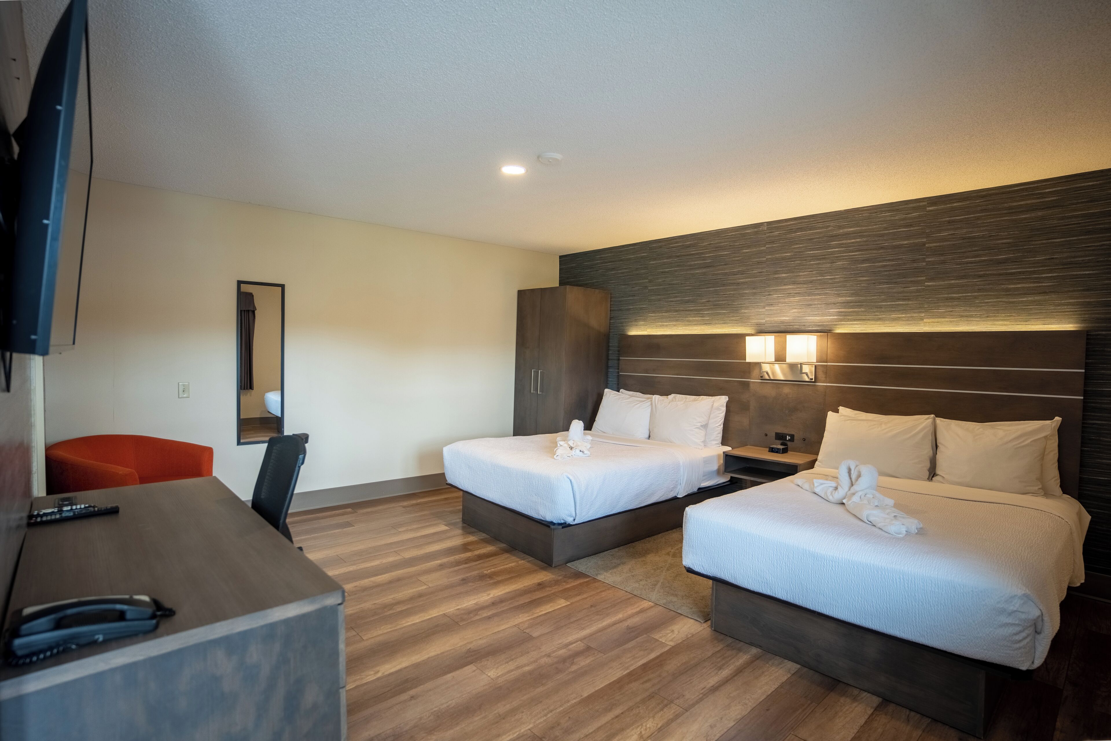 A hotel room with two beds, a desk, a chair, and a TV.