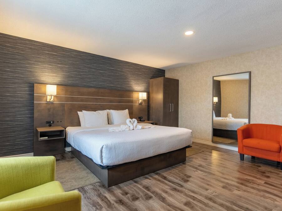 A modern hotel room with a large bed, a nightstand, a mirror, and a bright orange chair.