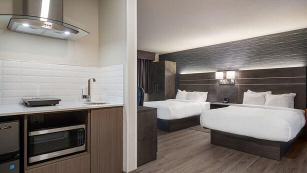 Une chambre d’hôtel dotée d’une kitchenette, de deux lits, d’un grand miroir et d’un design moderne.