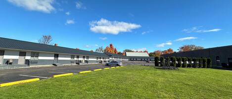 A motel with a parking lot, a grassy area, and a clear blue sky.