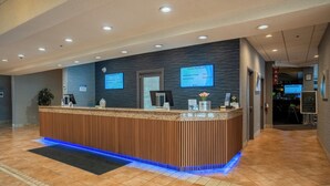 Un comptoir d’accueil avec un revêtement en bois et un éclairage à DEL bleuté. Deux écrans sont fixés au mur et affichent des informations.