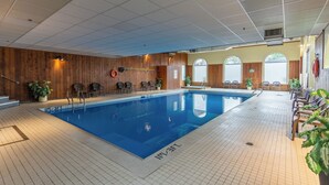 Une piscine intérieure avec des panneaux de bois, des espaces aménagés pour s’asseoir et des plantes en pot.