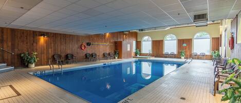 An indoor swimming pool with wooden paneling, seating areas, and potted plants.