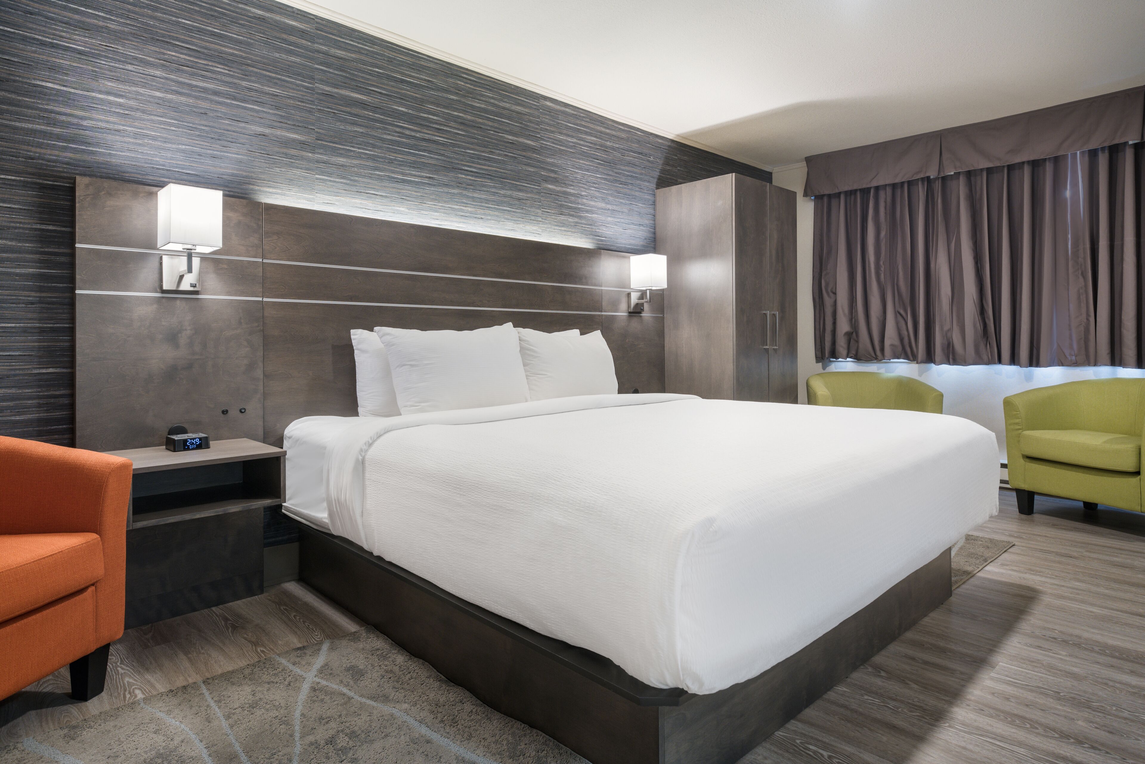 A modern hotel room with a large bed, two bedside tables, a nightstand, a desk, a chair, and a window with curtains.