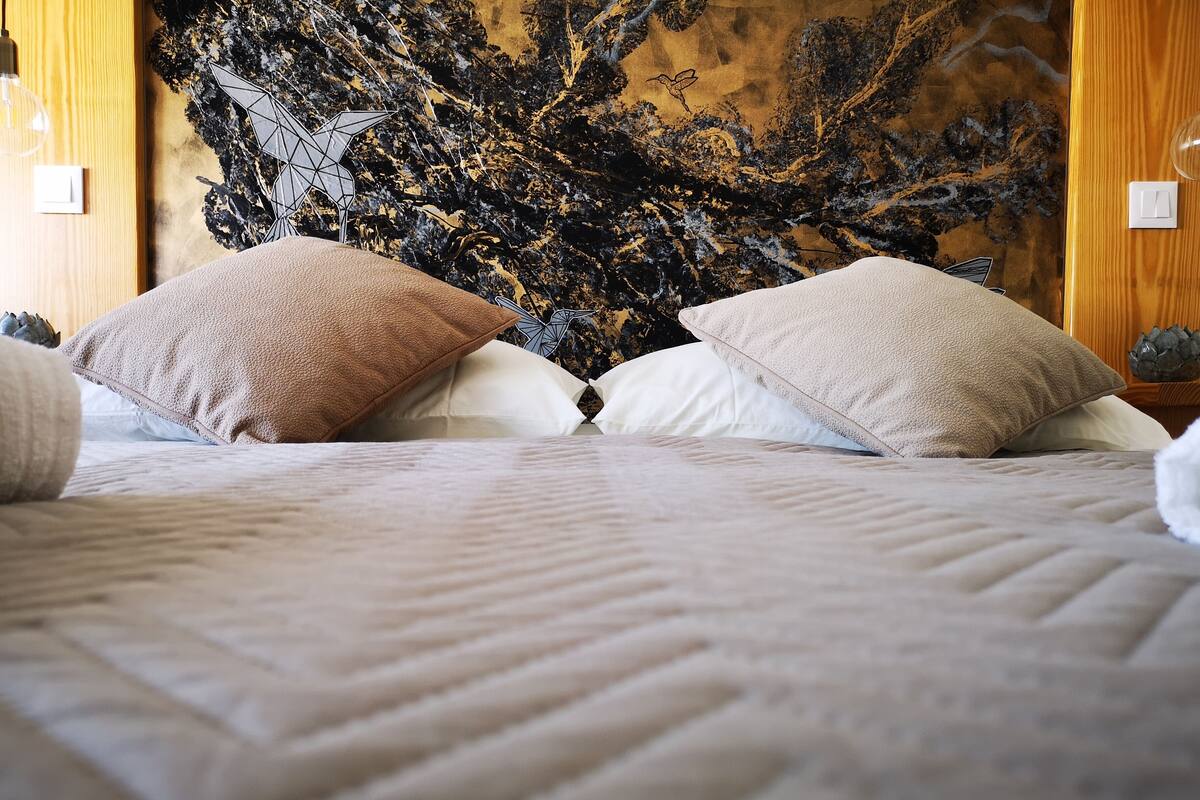 Una cama bien hecha con un edredón blanco texturizado, dos almohadas color beige y un mural decorativo en la pared.