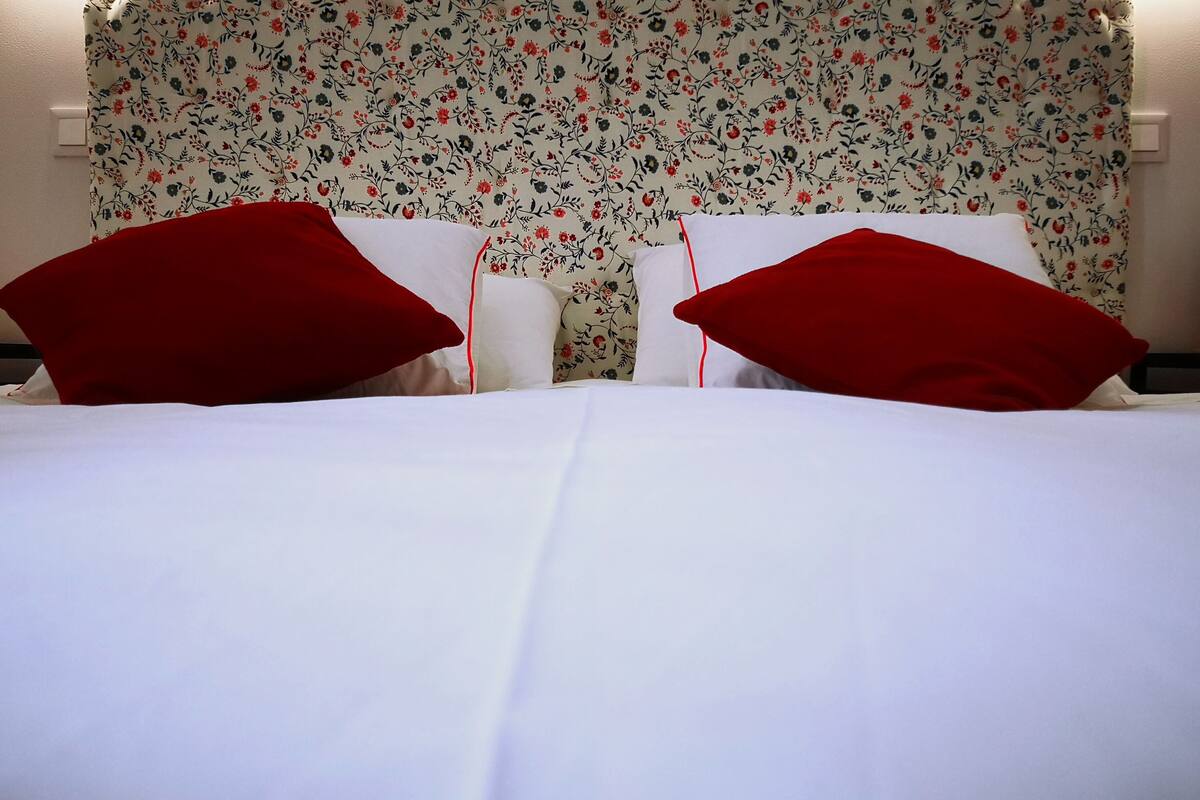 Una cama bien hecha con sábanas blancas y dos almohadas rojas.