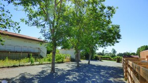 A fenced outdoor area with trees, a building with a red roof, and a gravel path. - Le Carbet Vendéen (Bouille-Courdault)