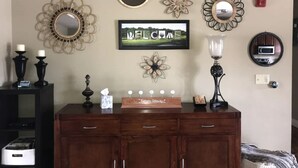 Une pièce avec un meuble en bois, des miroirs décoratifs, un panneau d’accueil et une petite table sur laquelle sont disposés des bougies et une boîte de mouchoirs.