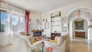 A spacious living room with a fireplace, white sofas, a coffee table, and a glass side table with a book. - 2947 Aia del Convento by BarbarHouse (Marittima)