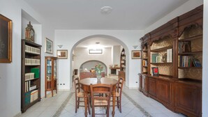 A dining area with a round table and chairs, flanked by wooden bookshelves and a decorative cabinet. - 2947 Aia del Convento by BarbarHouse (Marittima)