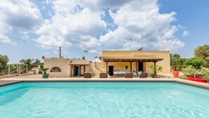 Une piscine avec un espace patio, un bâtiment en pierre et un espace de détente couvert, équipé de tables et de chaises.
