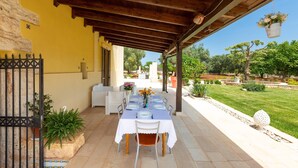 Une terrasse extérieure avec une table dressée pour le repas, entourée de plantes en pot et d’un mur de pierre.