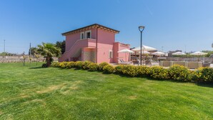 A pink building with a small staircase, surrounded by a well-maintained lawn and yellow flowers.