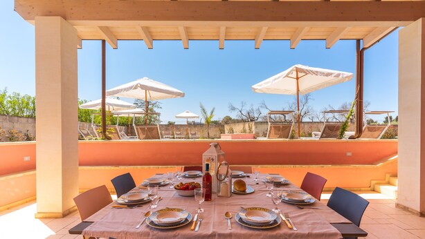 An outdoor dining area with a table set for four, surrounded by chairs, under a wooden pergola.