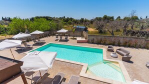 A rooftop pool area with lounge chairs and umbrellas, surrounded by a stone wall and trees.