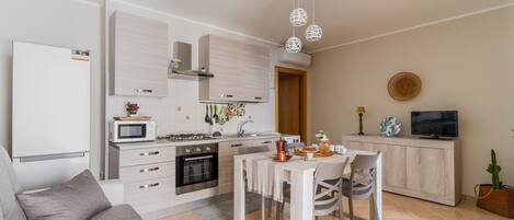 Una cocina moderna con armarios blancos, microondas, estufa y un lavamanos. Hay una mesa de comedor con sillas y un sofá en la sala de estar.