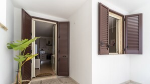 A hallway with a potted plant, a door with brown shutters, and a tiled floor.
