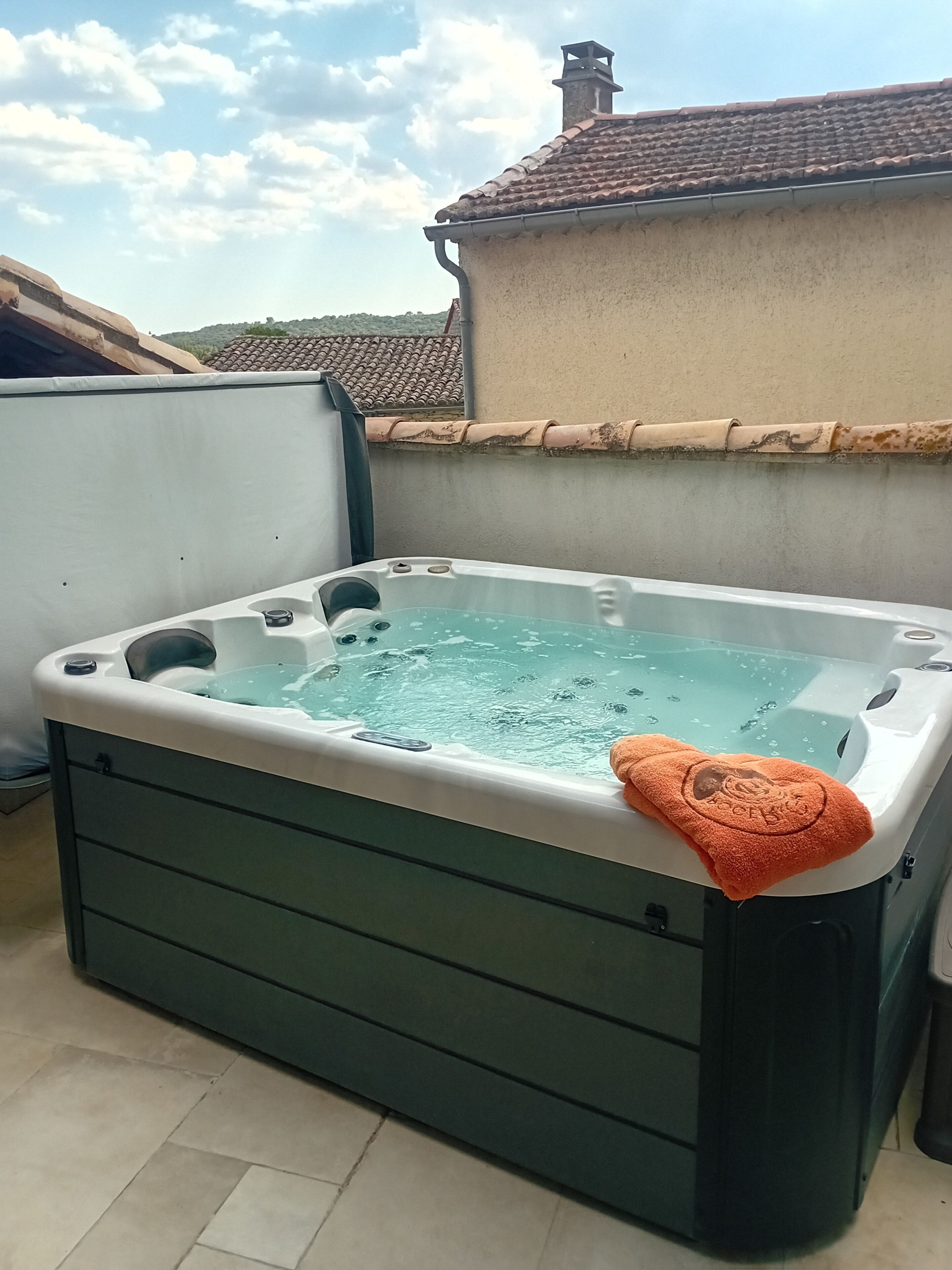 Un jacuzzi sur un balcon avec vue sur un toit recouvert de tuiles et un immeuble.