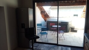 Een kleine keuken met een koelkast, een barstoel en een schuifdeur die uitkomt op een terras met een tafel en stoelen.