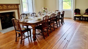 Comedor con mesa de madera dispuesta para seis personas, flanqueado por dos ventanas y una chimenea.